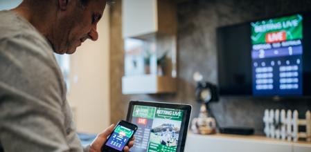 Mature man using mobile app for live betting and online gambling and watching a sports match
